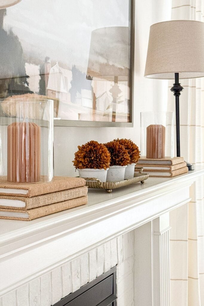 Winter mantel decorated with candles, stacked books, and simple neutral accessories beneath artwork