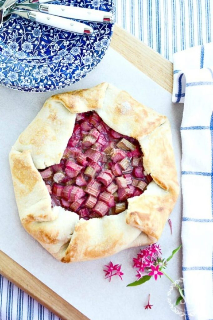 rhubarb galette on a cutting board with blue and white plates and white-handled utinsels