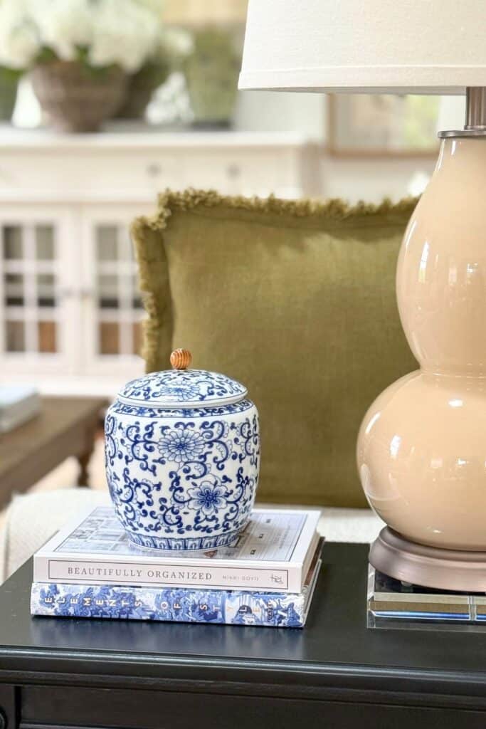 Blue and white ginger jar styled on stacked books beside a lamp on a black end table for budget friendly decorating.