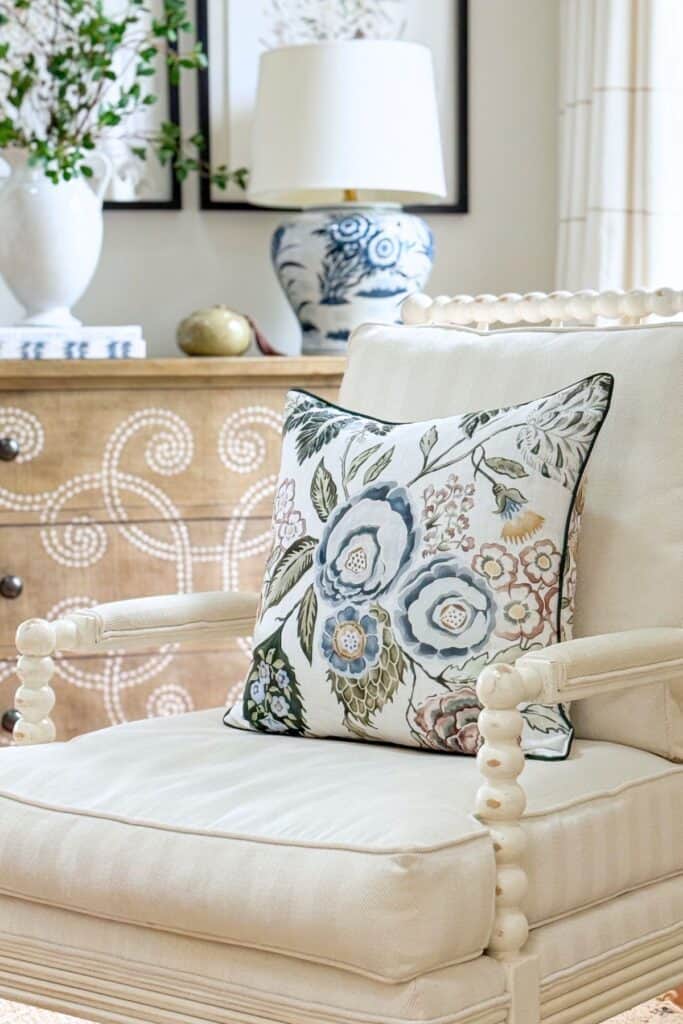 Cream accent chair styled with a floral decorative pillow in a neutral living room for budget friendly home decorating.