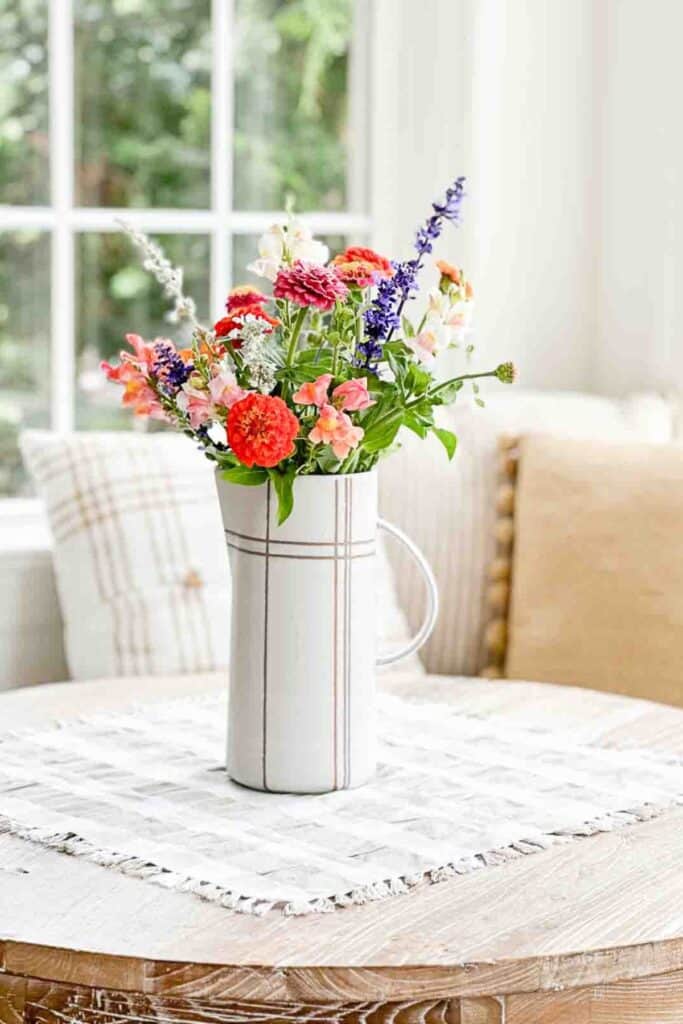 Colorful fresh flower arrangement in a white pitcher on a dining table for budget friendly home decorating.