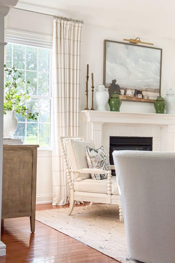 Neutral living room with green accents, layered pillows, greenery, and decorative ginger jars styled on a white fireplace mantel.