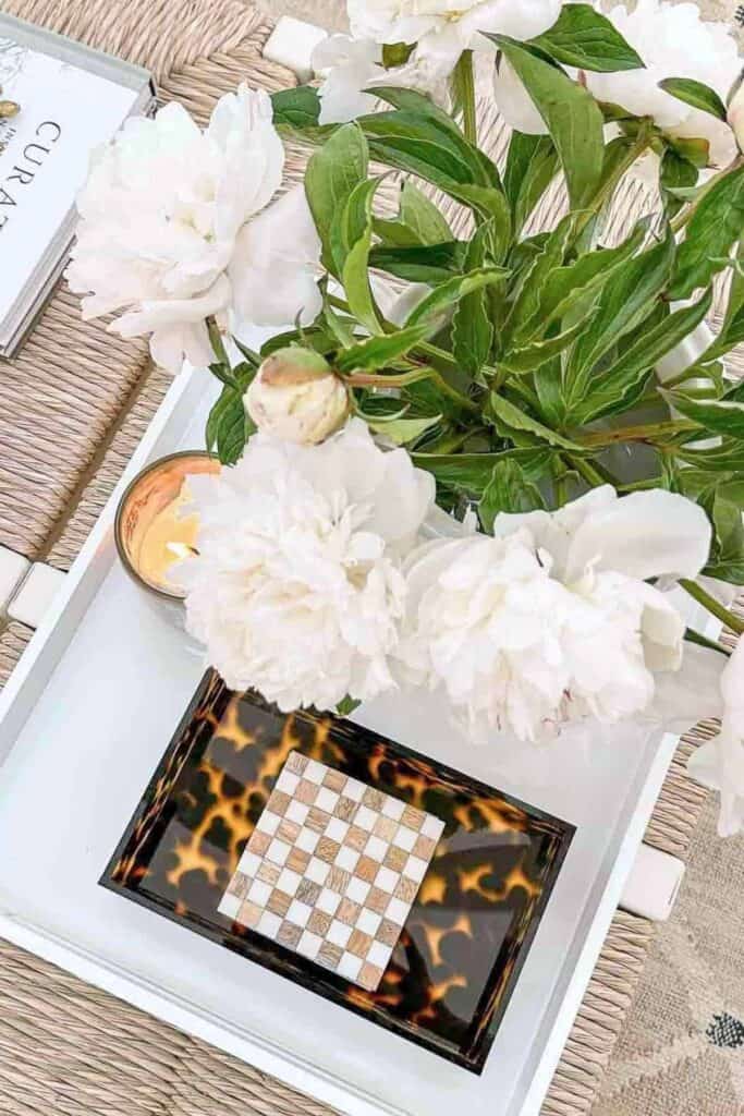 White peonies arranged on a tray with a candle, decorative box, and woven textures for budget friendly home decorating.