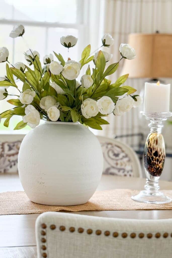 White floral arrangement in a round vase on a dining table with candleholders for budget friendly home decorating.