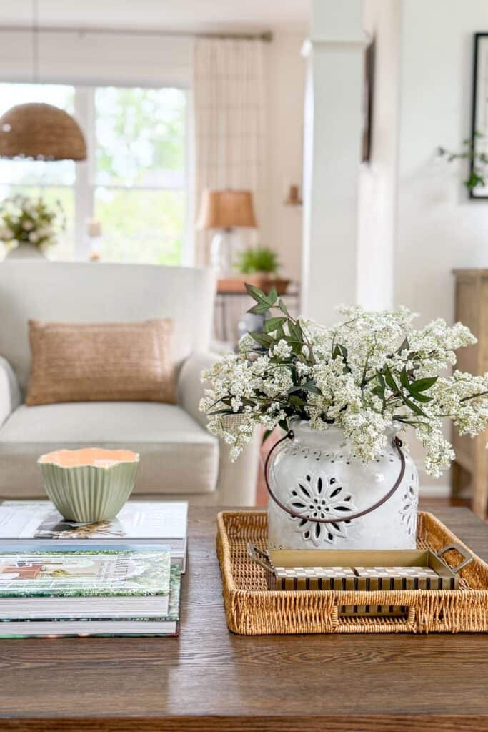 Coffee table vignette with books, a candle, a woven tray, and faux flowers styled using everyday home decor accessories.