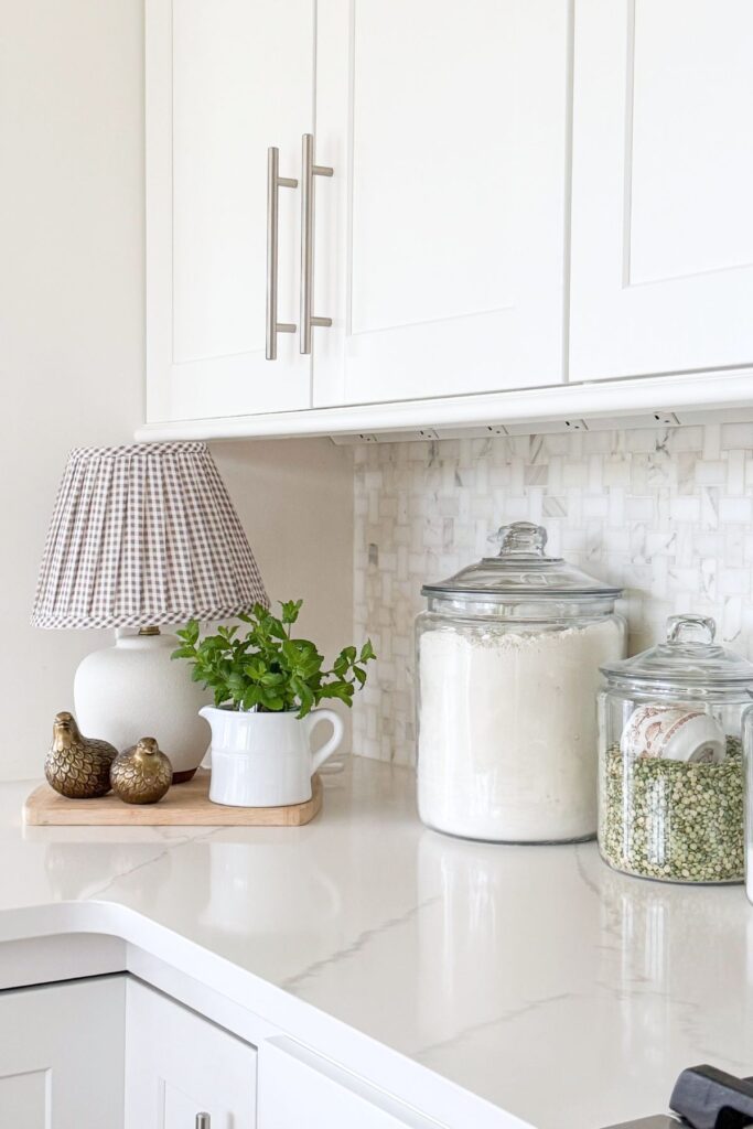 spring kitchen decorating ideas with counter corner styling, lamp, herbs in pitcher, and glass canisters