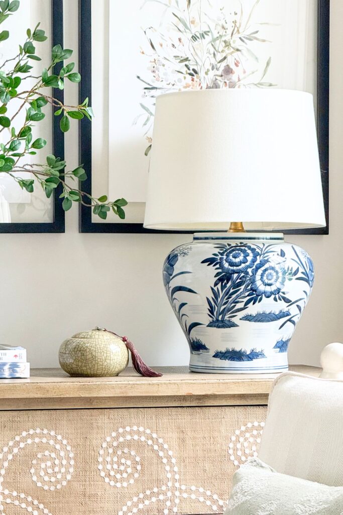 Blue and white ginger jar lamp styled on a console table with a small decorative box and framed botanical art