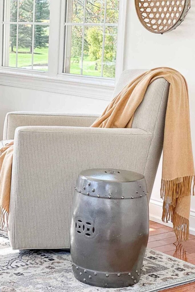 Metal garden stool used as a small drink table next to a swivel chair with a camel throw in a cozy winter sitting area.