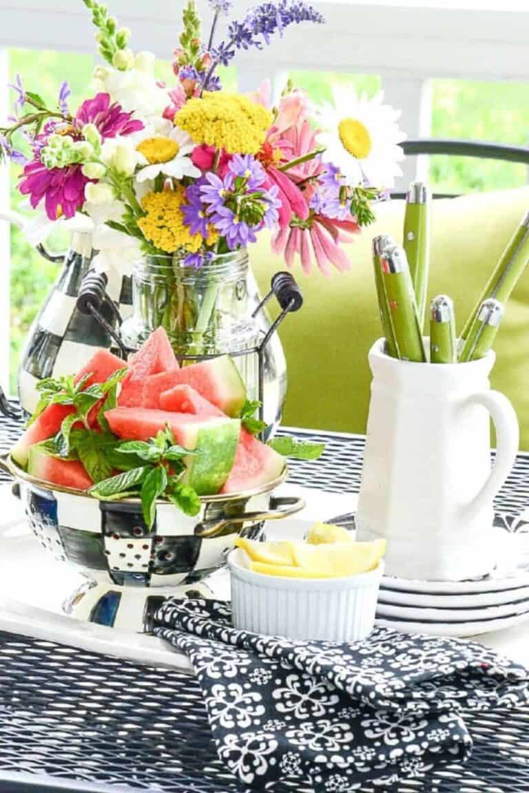 summer flowers in a mason jar with a bowl of watermelon on an outdoor table