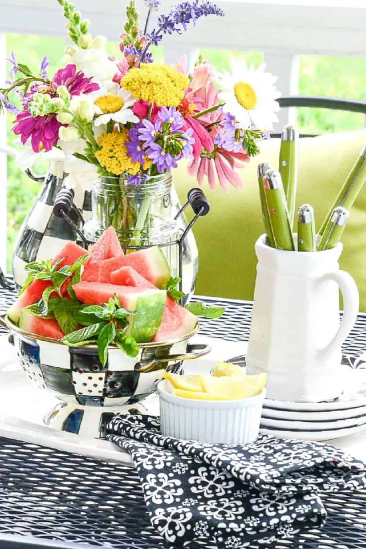 summer flowers in a mason jar with a bowl of watermelon on an outdoor table