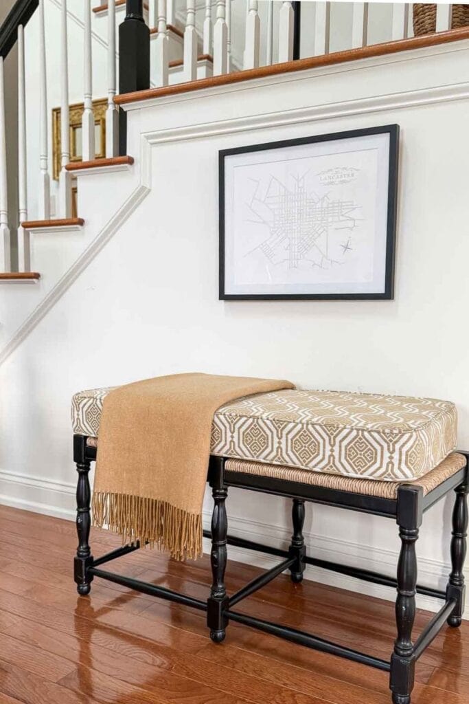 Upholstered bench with patterned cushion and camel throw styled under a staircase in a warm winter foyer.