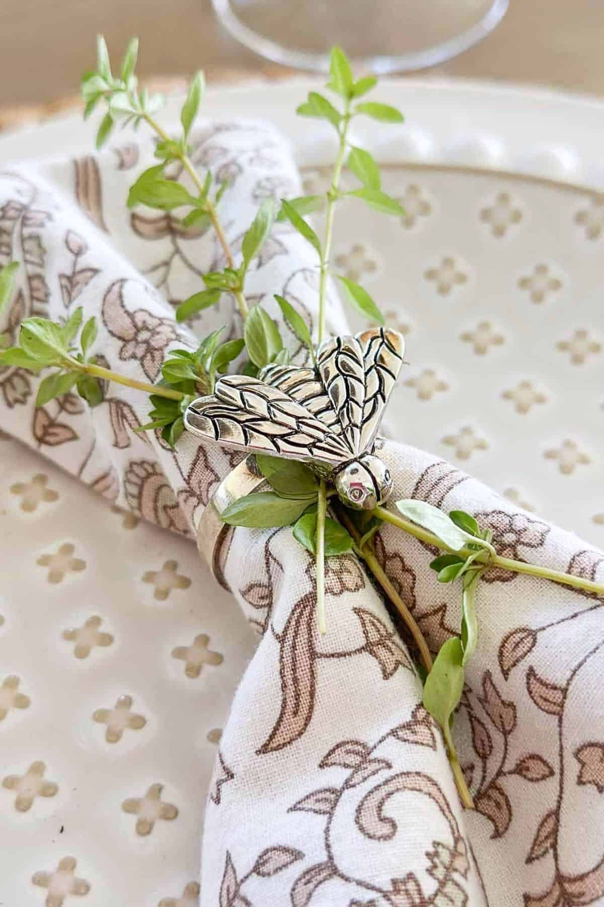 place setting with a bee napkin ring and sprigs of fresh oregano