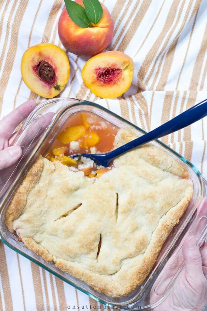 peach cobbler in a glass baking dish on a towel with fresh peaches