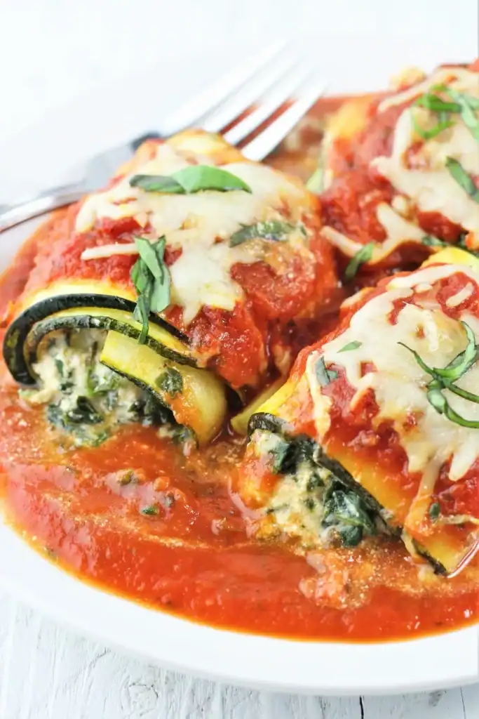 zucchini rolls on a plate swimming in tomato sauce