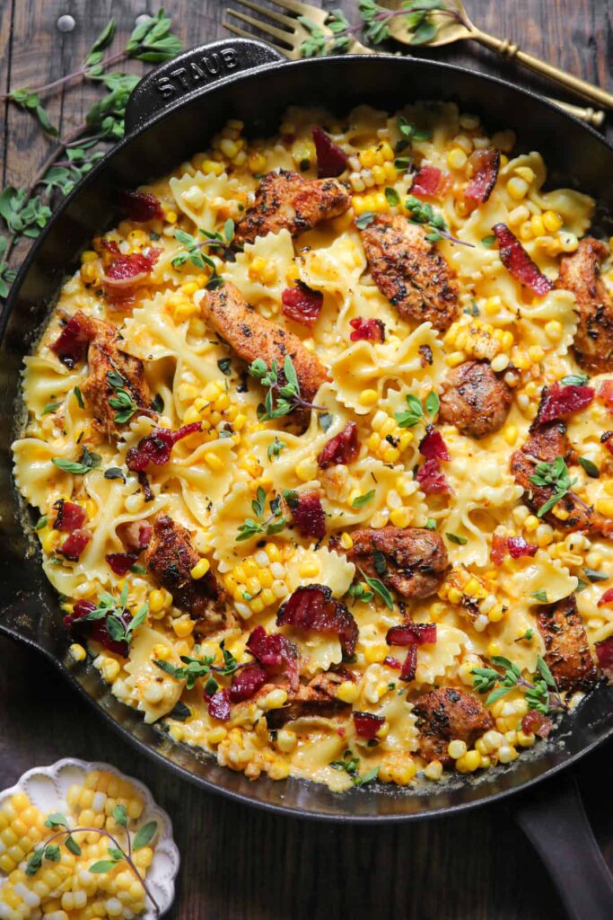 iron skillet filled with chicken creamy corn and bacon bits surrounded by herbs