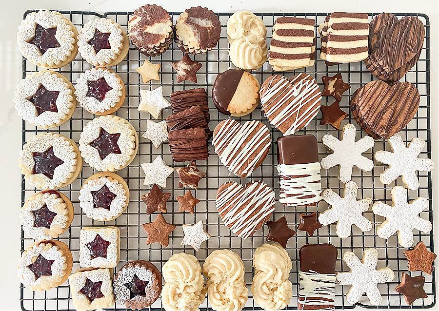 Assorted Christmas cookies on a cooling rack, including heart cookies, star cookies, snowflake cookies, and chocolate dipped cookies.