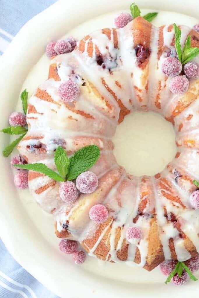 Cranberry orange bundt cake drizzled with glaze and topped with sugared cranberries and fresh mint.