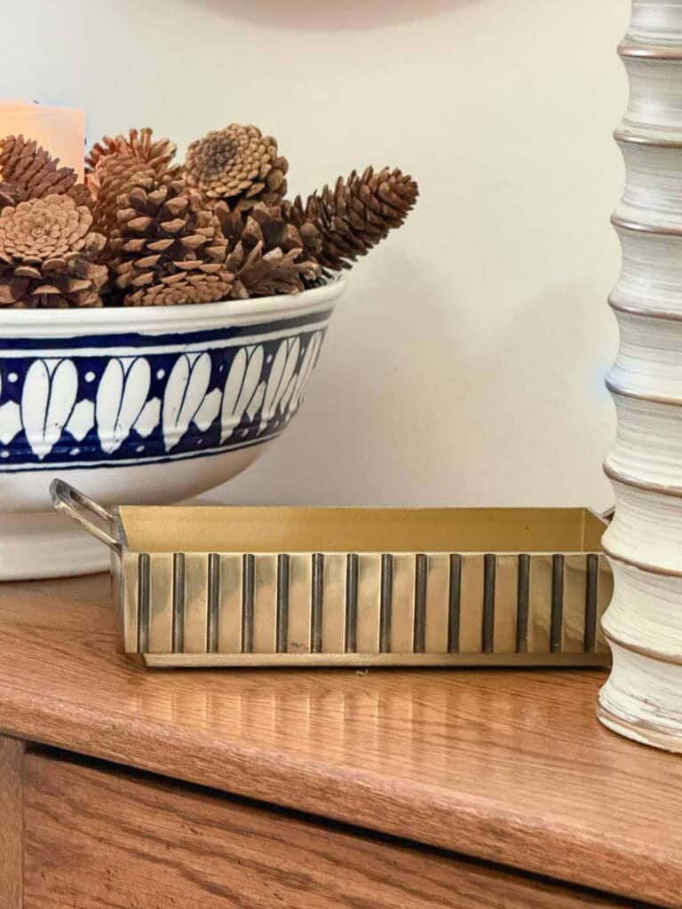 Winter foyer decor with a bowl of pinecones and a brass trinket container styled on a console table for a warm and welcoming entryway.