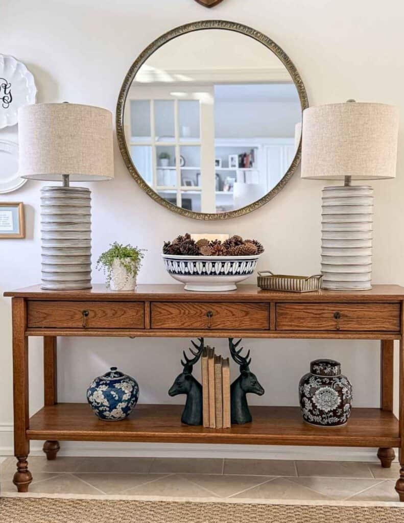 foyer table with a pair of lamps, a bowl of pinecones decorated for winter