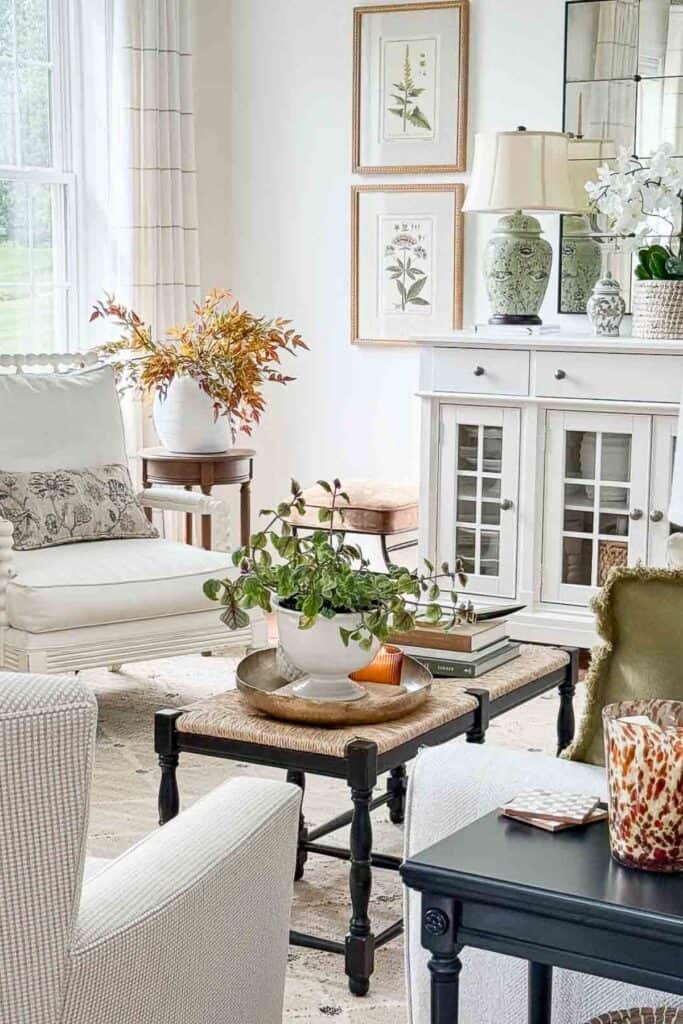 Bright living room with white armchair, framed botanical prints, and coffee table styled with a tray, greenery, and candle.