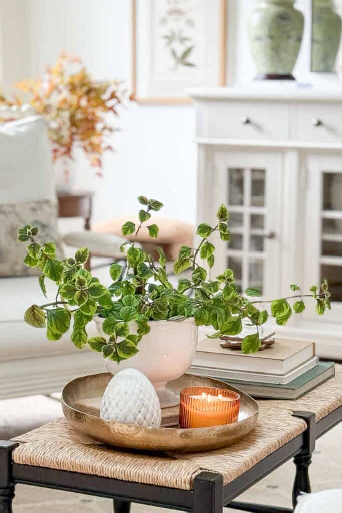 Coffee table decorated with greenery in a white vase, a lit candle, and decorative accents with fall leaves and artwork in the background.