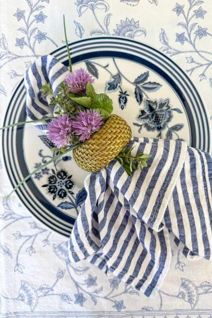 blue and white spring place setting with striped napkin, woven napkin ring, and fresh purple flowers