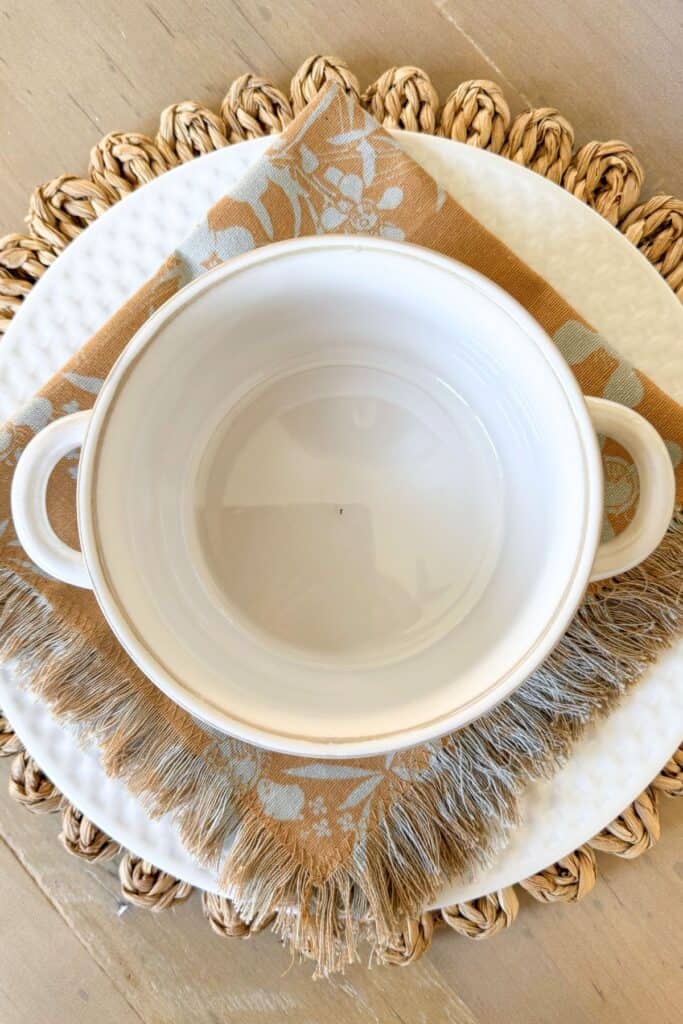 Spring table setting with woven placemats, neutral patterned napkins and white soup bowls layered on white plates
