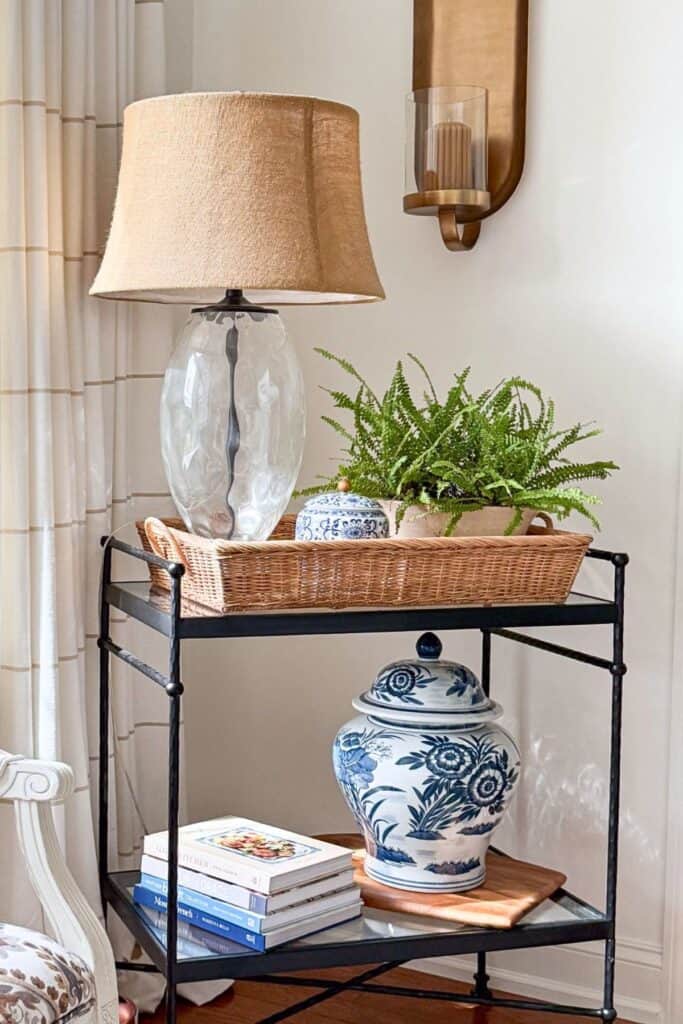 Two tier bar cart styled with lamp, fern, blue and white ginger jars, and stacked books showing the rule of three