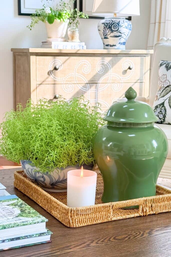 Coffee table vignette with green ginger jar, plant, and candle on a woven tray showing the rule of three