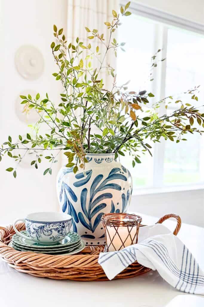Layered vignette with stacked teacups, woven candle, and blue and white vase showing the rule of three