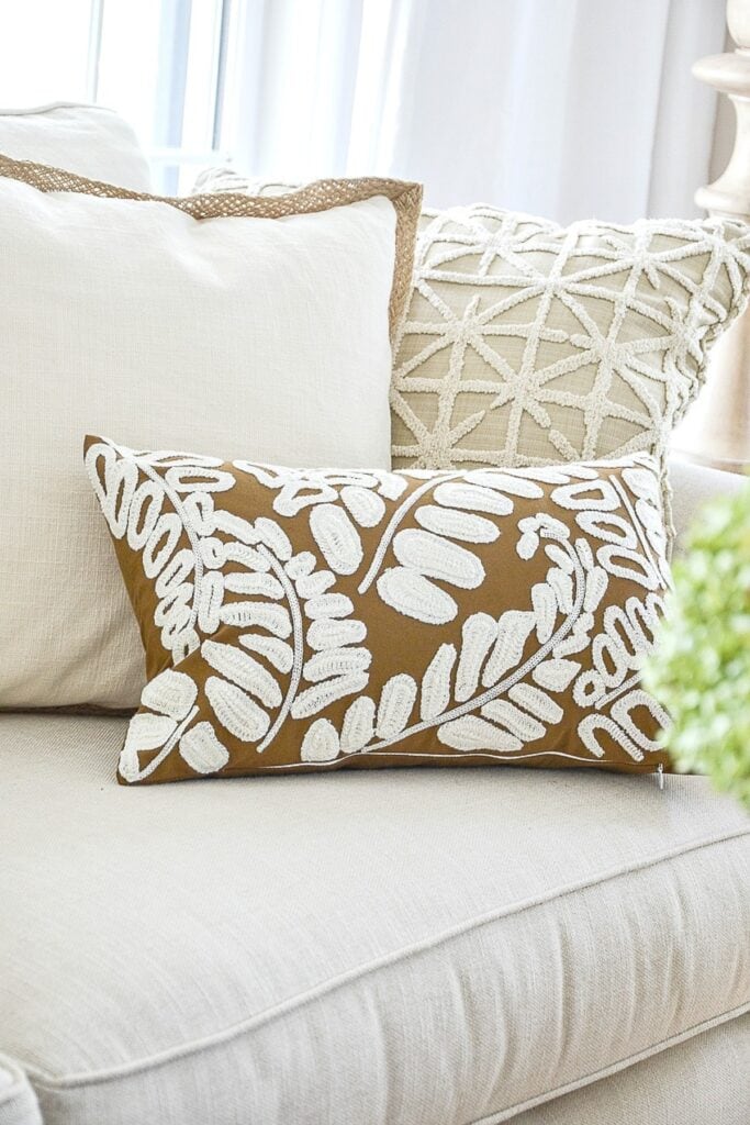 Three pillows in varying sizes and textures on a sofa showing the rule of three, cream jute trim pillow, textured lumbar, and patterned leaf pillow