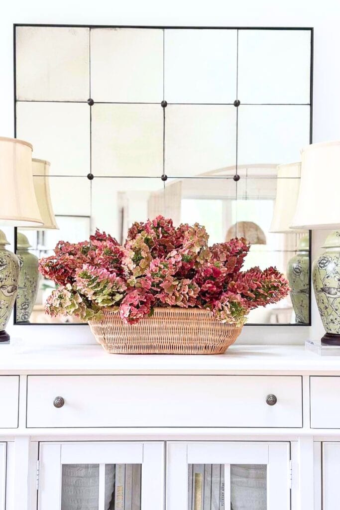 Single vase of greenery on a woven tray on a mantel, a simple standalone decor moment