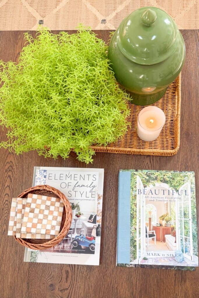 Overhead view of coffee table styled with stacked books, woven basket of coasters, and a rule of three vignette
