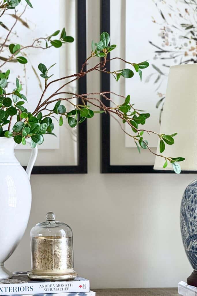 Console table vignette with white pitcher of greenery, mercury glass cloche on books, and blue and white lamp showing the rule of three