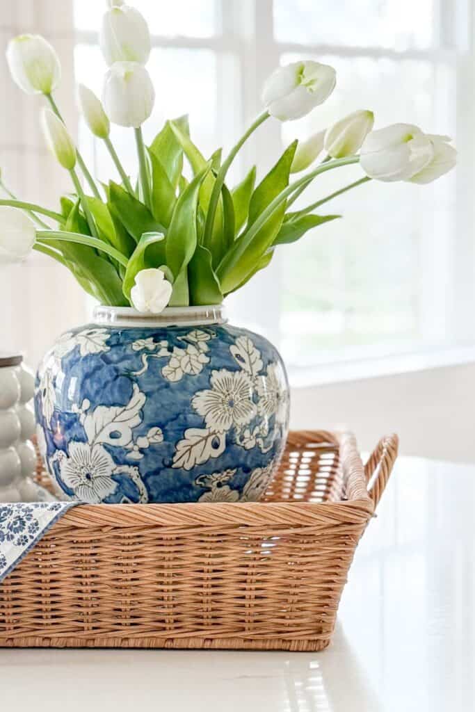 blue and white vase with white tulips on woven tray in bright kitchen
