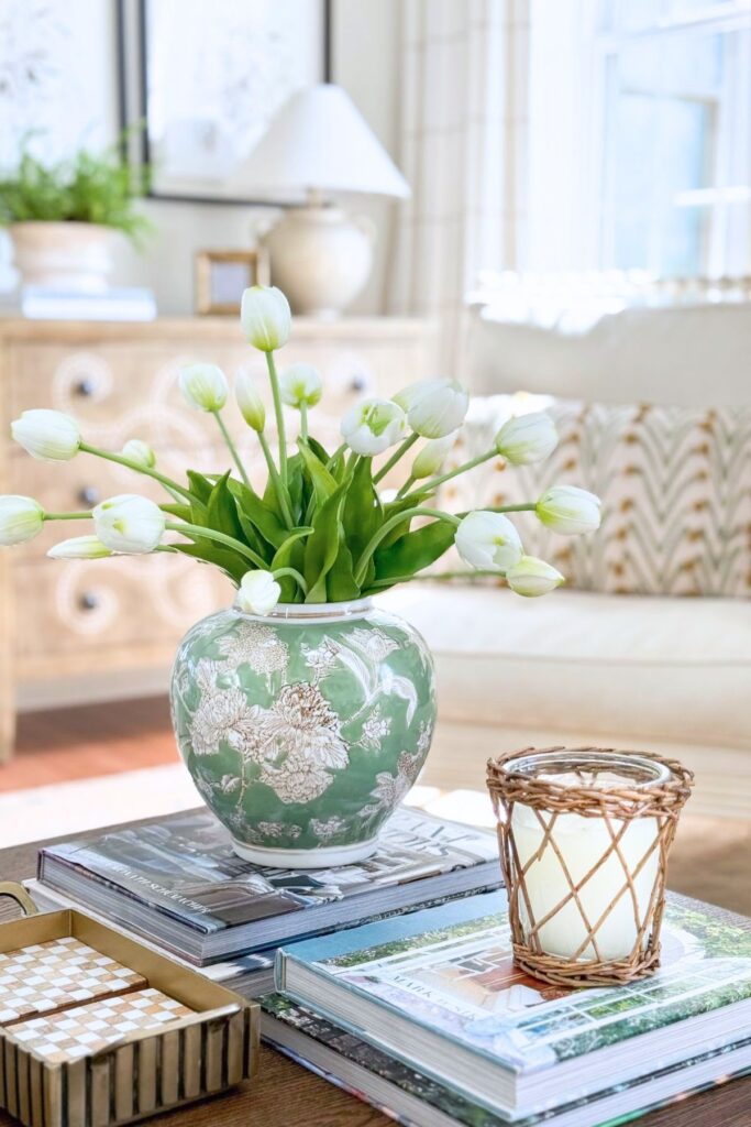 coffee table styled with books, floral arrangement in vase, and candle in neutral living room