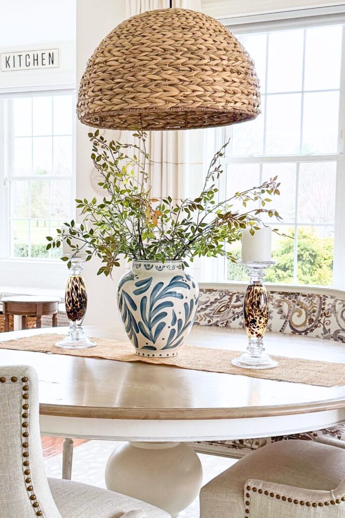 round dining table styled with vase of greenery, candles, and woven pendant light