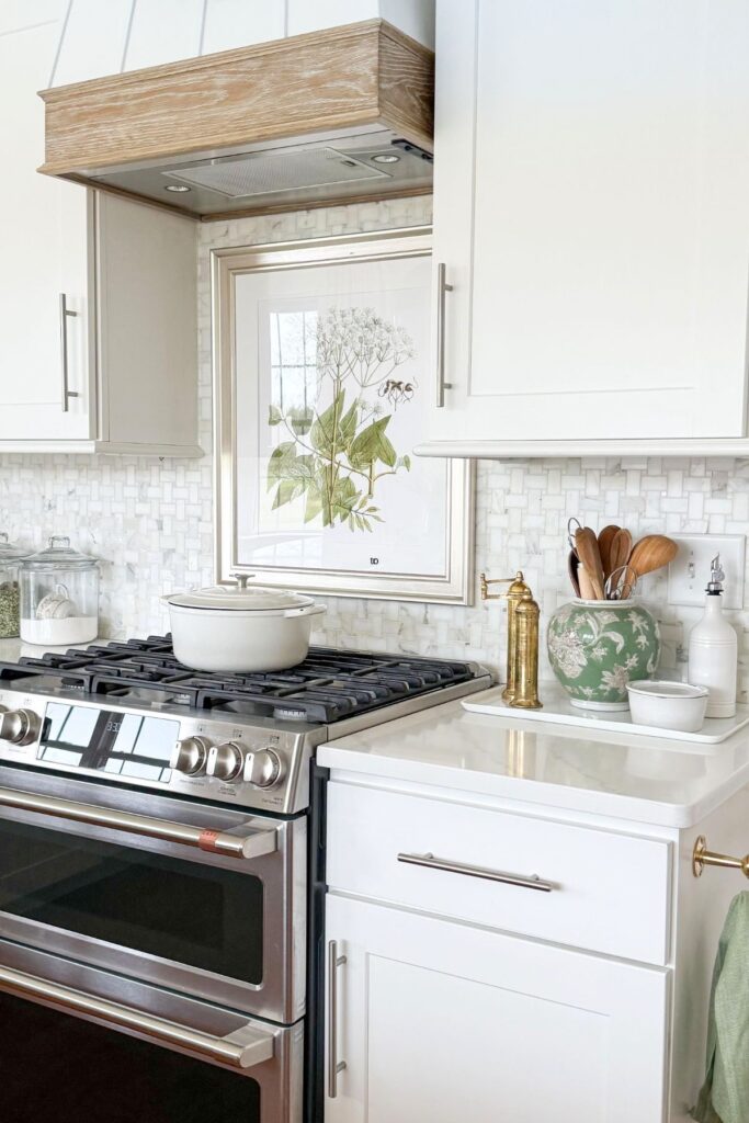 kitchen counter styled with tray, utensils, green vase, and framed botanical art