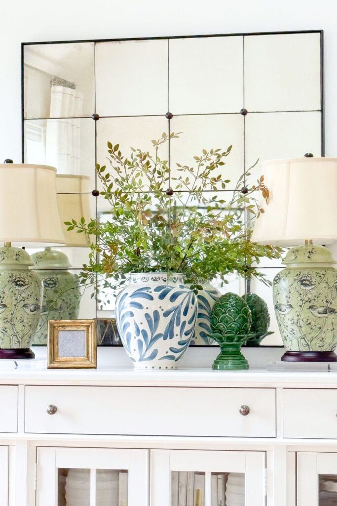 console table styled with mirror, lamps, and blue and white vase with greenery