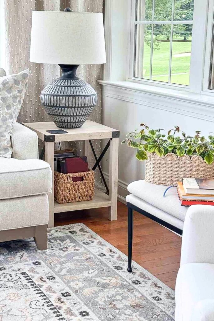 ottoman used as a side table with lamp and basket next to chair with area rug and plant in living room