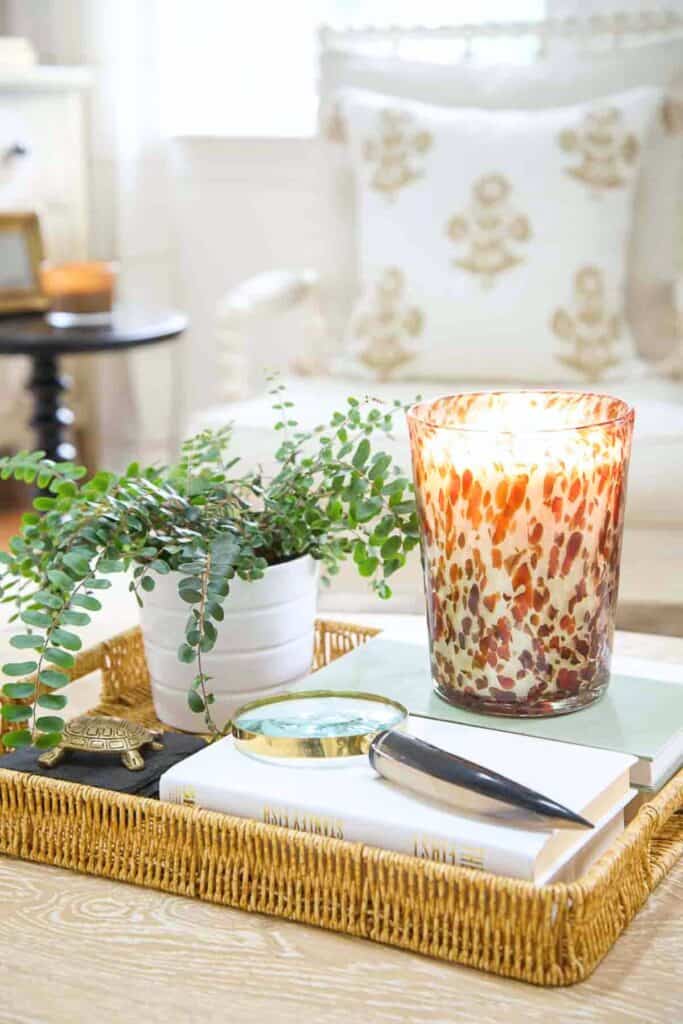 woven tray styled with books, candle, greenery, and decorative accessories on coffee table
