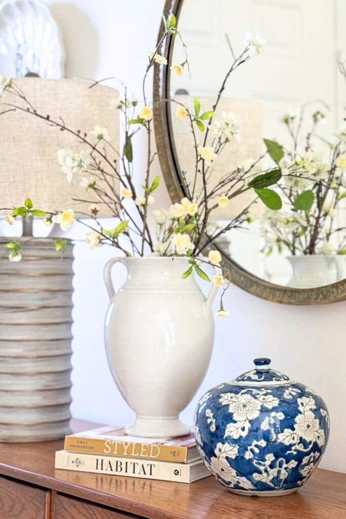 console table styled with vase of branches, stacked books, and decorative blue and white jar