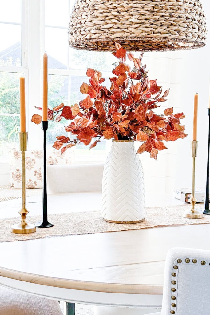 A CENTERPICE WITH BURNT ORANGE BRANCES OF LEAVES FLANKED BY CANDLESTICKS