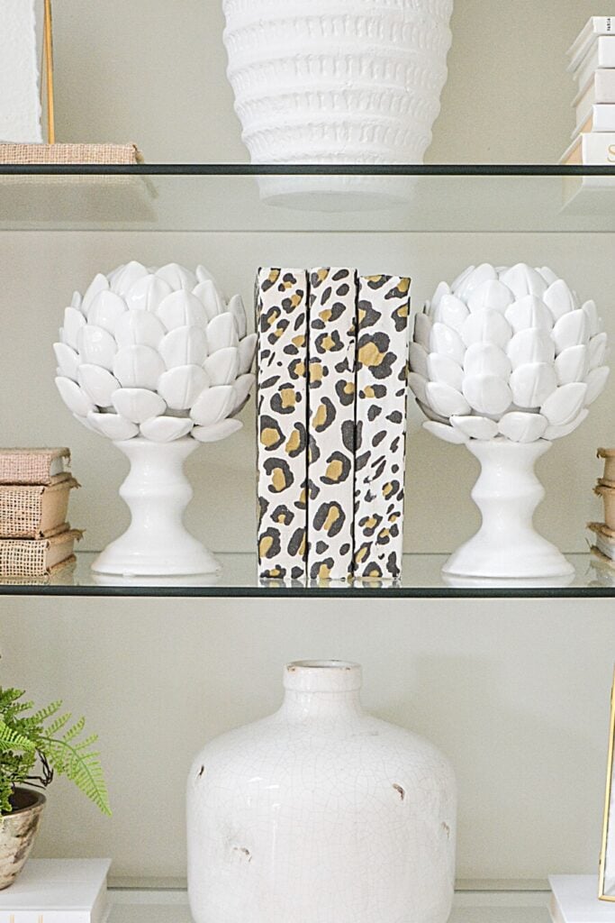 stack of books styled with decorative artichoke bookend on bookshelf