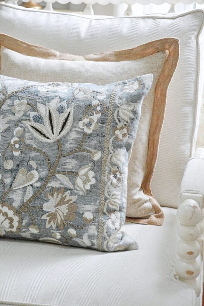 Warm neutral chair with beige pillows layered with a blue gray accent pillow showing how to mix warm and cool colors in decorating
