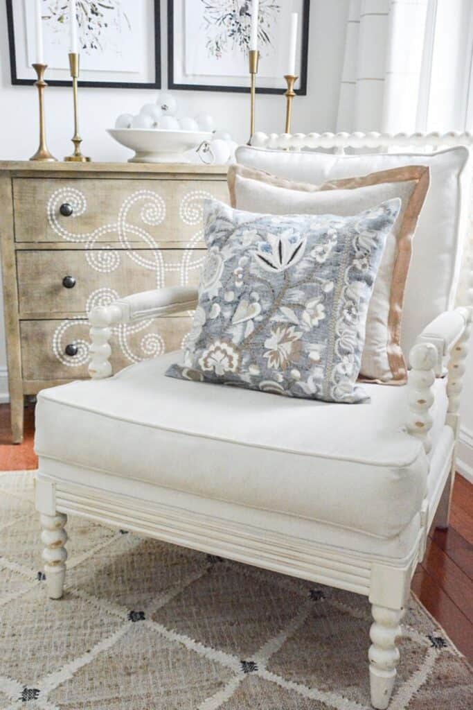 Warm neutral accent chair with beige pillows and a blue gray patterned pillow showing how to mix warm and cool colors in decorating
