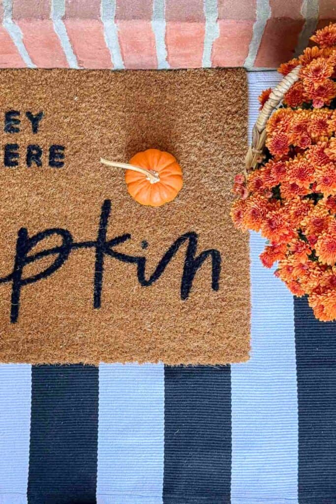 pumpkin on a door mat with a black and white striped rug under it