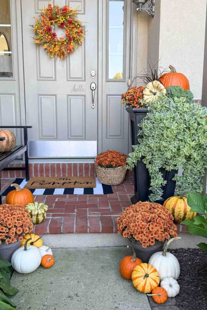 pumpkins and a gourd with a potted mum spill off the front porch and next to the waldway