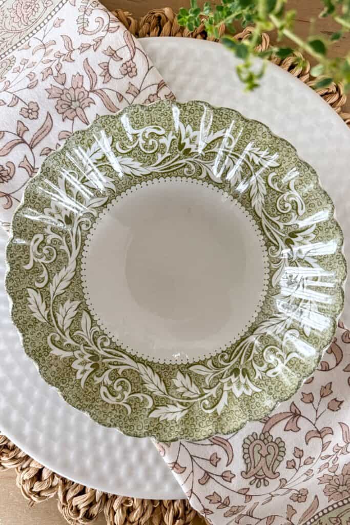green vintage patterned bowl layered on white plate with woven placemat and floral napkin