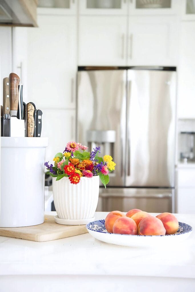 bowl of peaches and flowers on a kitchen counter